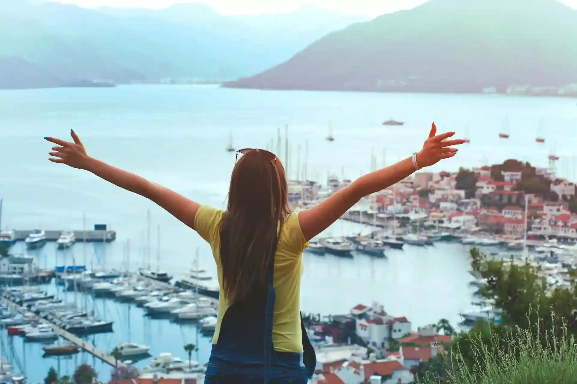 Traveler with arms outstretched overlooking a scenic coastal town, symbolizing the freedom and ease that travel apps can bring to your journey.