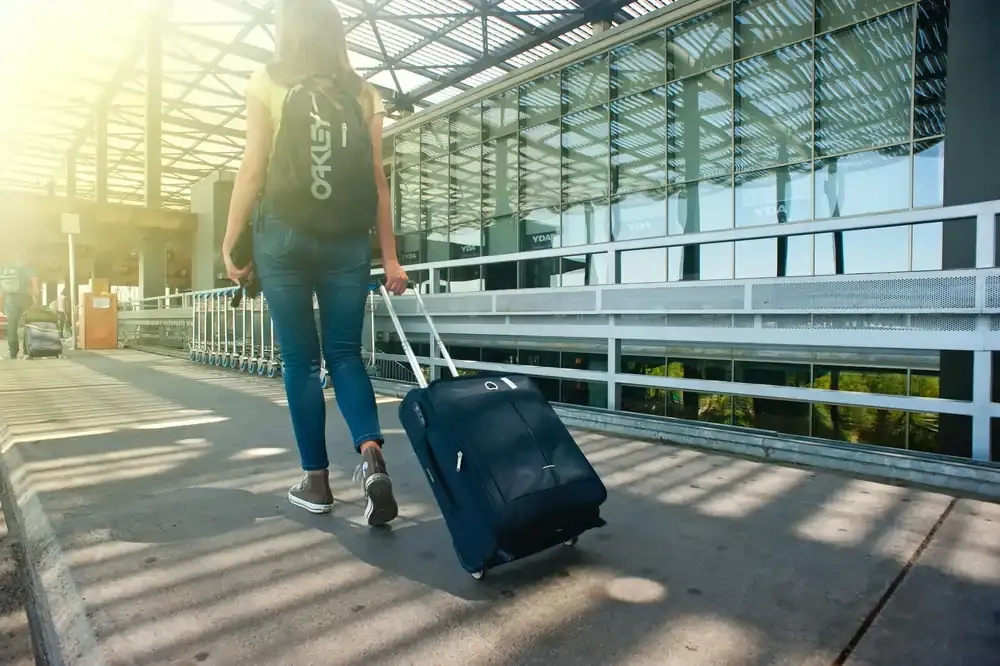 Person with backpack and rolling luggage approaching an airport.