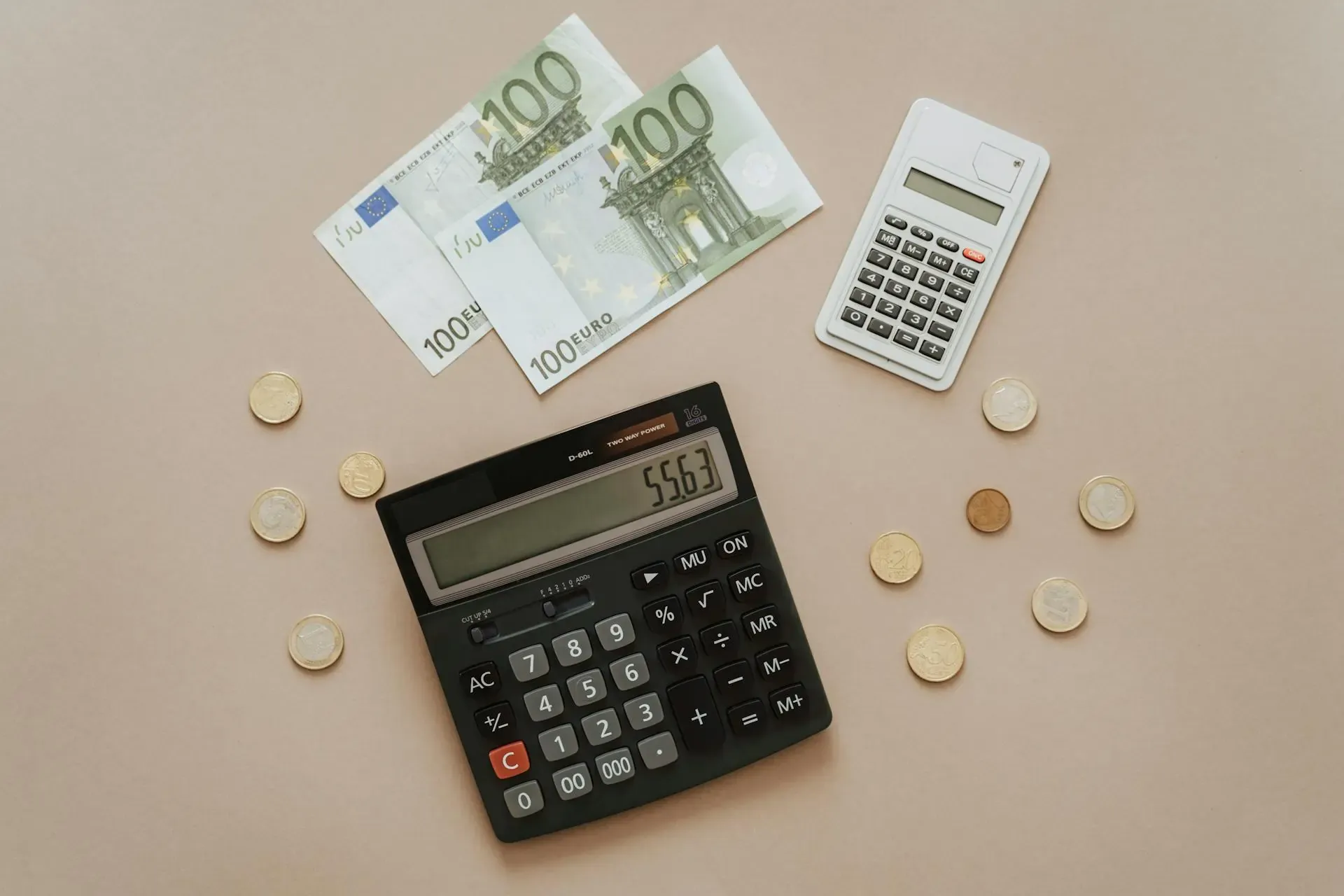 Two calculators, Euro banknotes, and coins laid out on a neutral background.