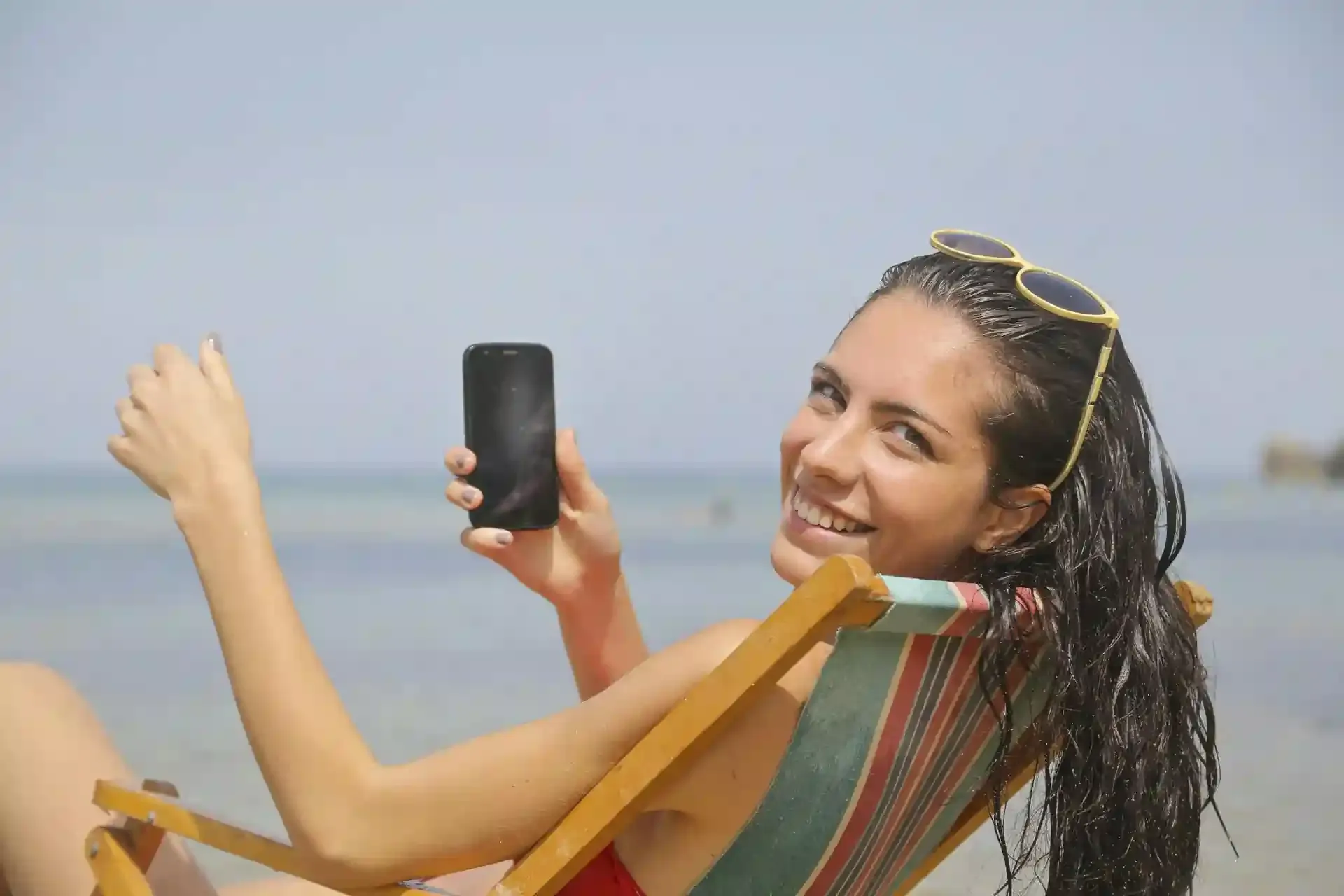 Beach vacationer holding up her mobile phone, representing staying connected overseas without roaming charges.