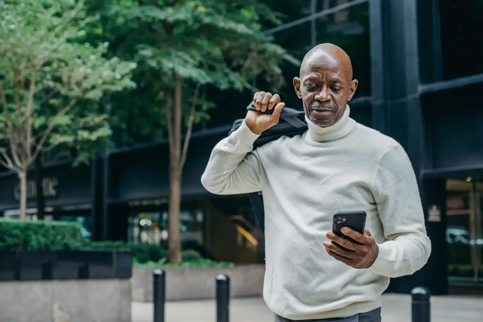 Man standing outdoors in an urban setting, holding a smartphone and checking his messages, possibly using mobile data or an eSIM for international connectivity.