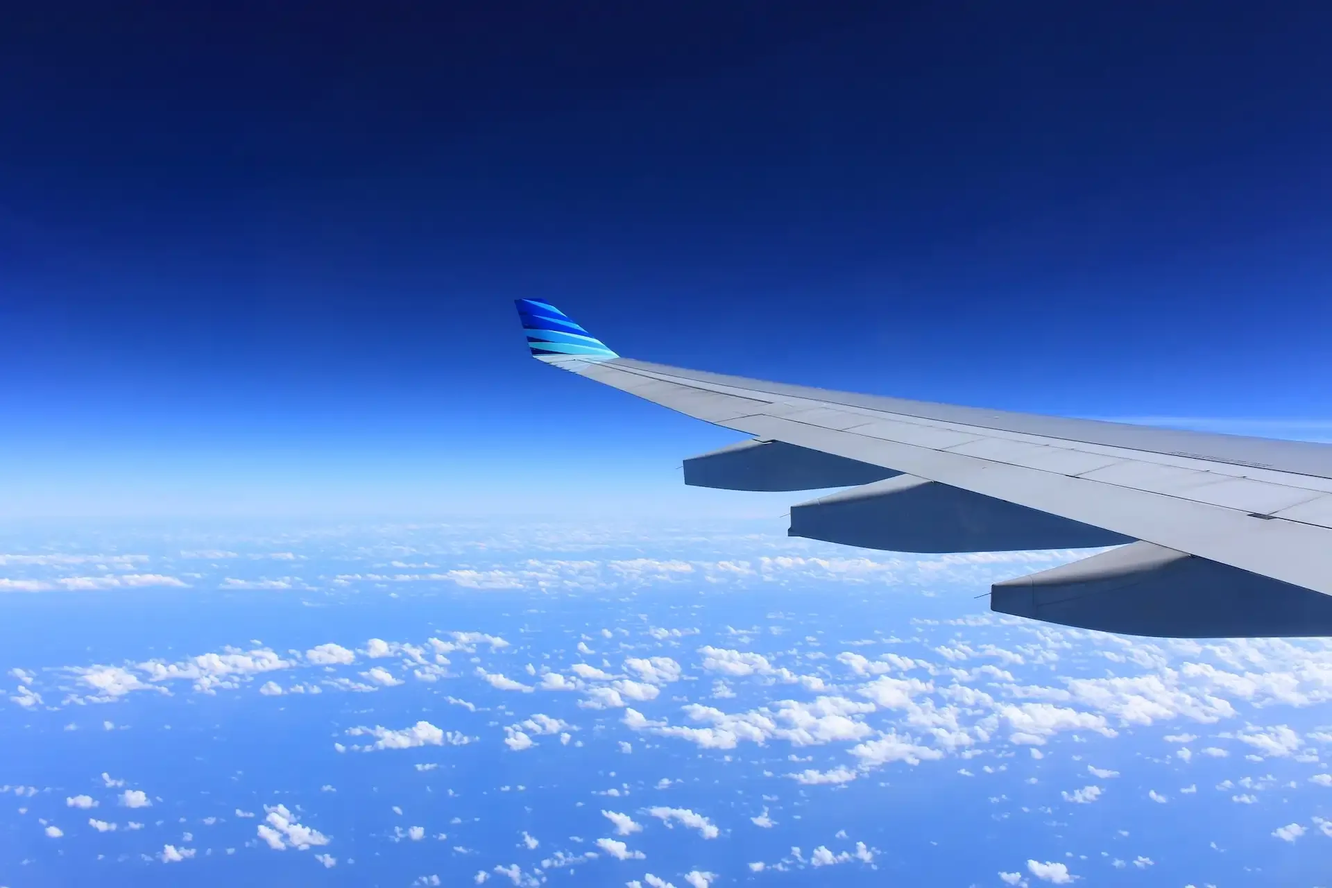 View of airplane wing above the clouds during flight, representing long-haul travel and the need for engaging ways to stay entertained onboard.