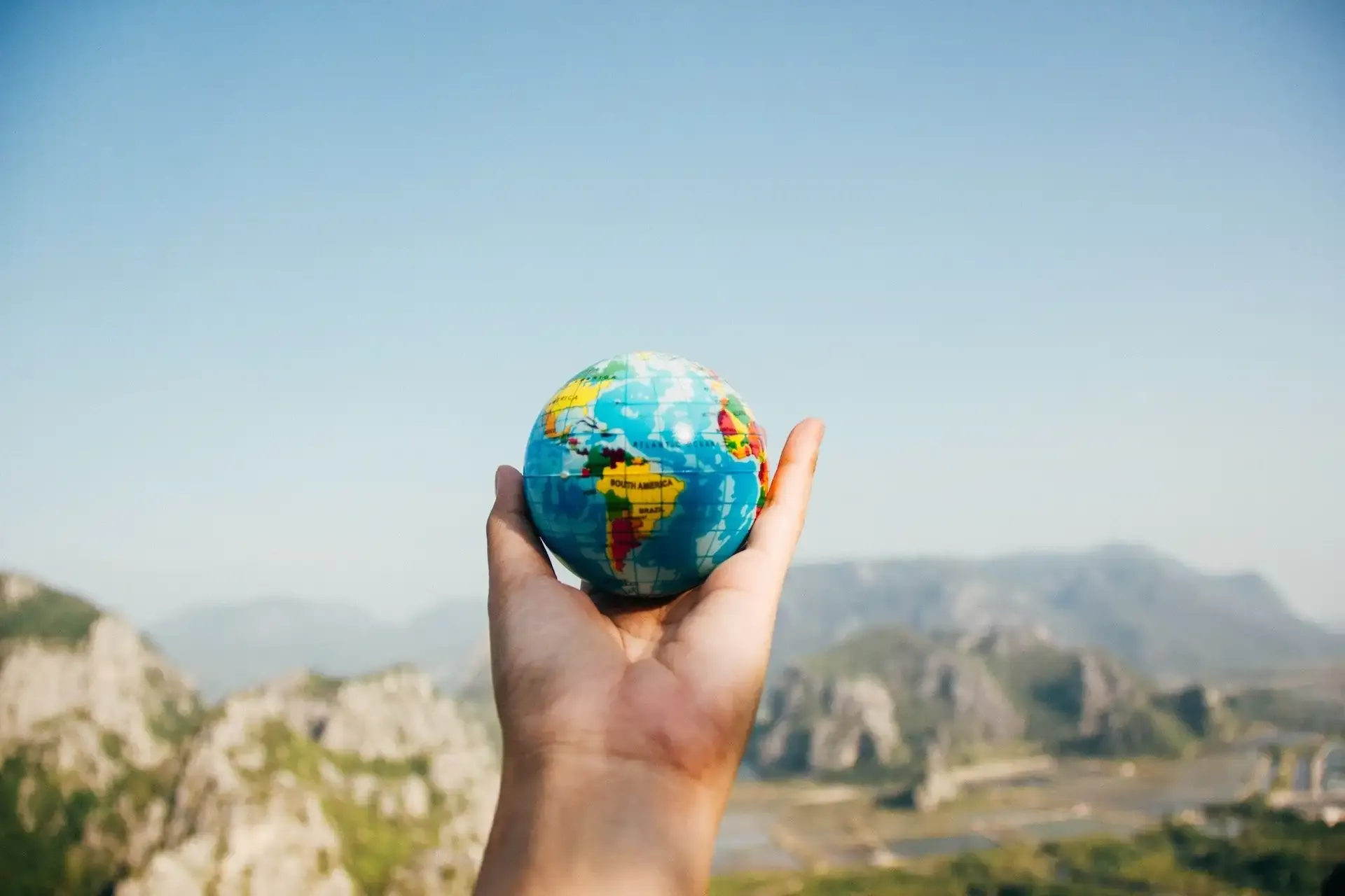 Hand holding a small globe with a mountainous landscape in the background — symbolic image for international travel, roaming, and global connectivity.