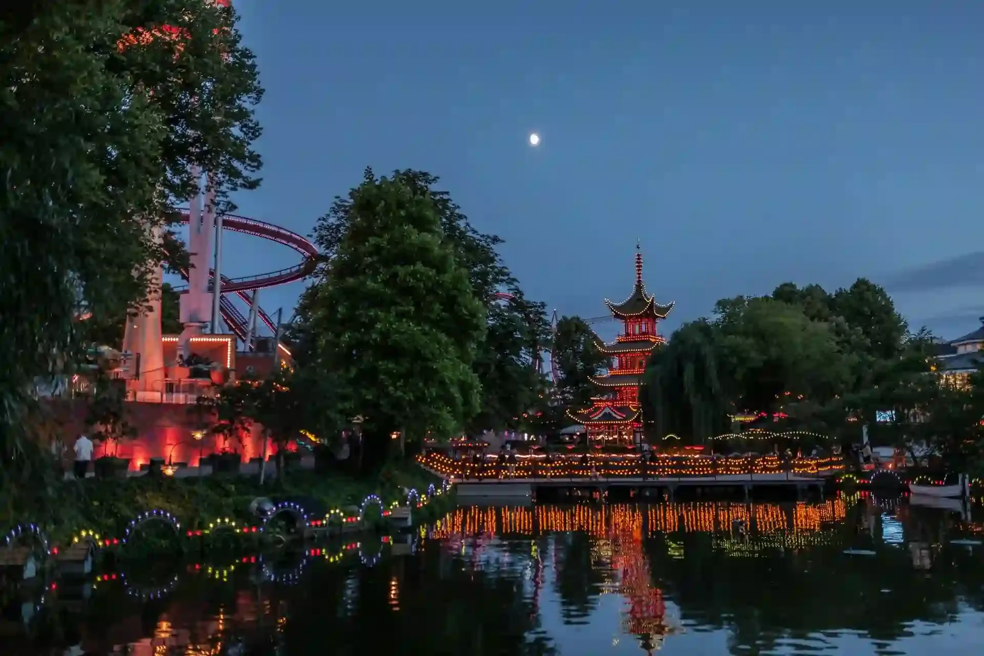 Tivoli Gardens amusement park in Copenhagen lit up at night, with reflections of colorful lights and a pagoda on the water—an enchanting family-friendly travel destination.