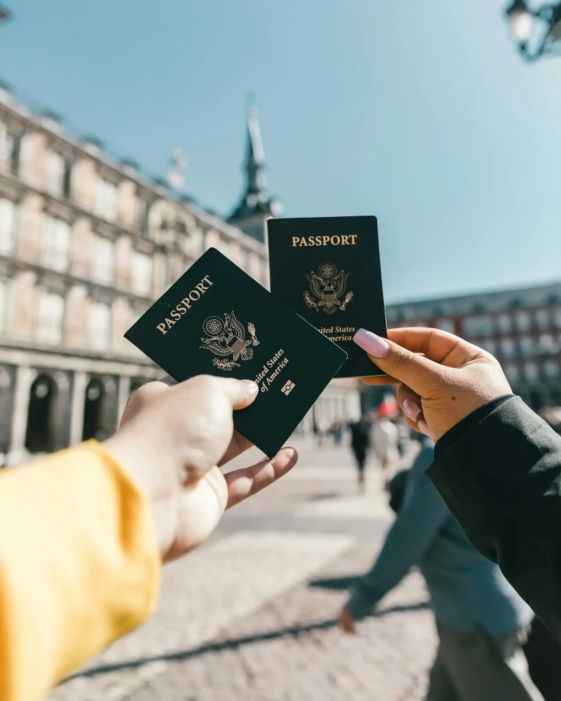Two travelers holding U.S. passports in a European plaza, exploring alternatives to Verizon Travel Pass