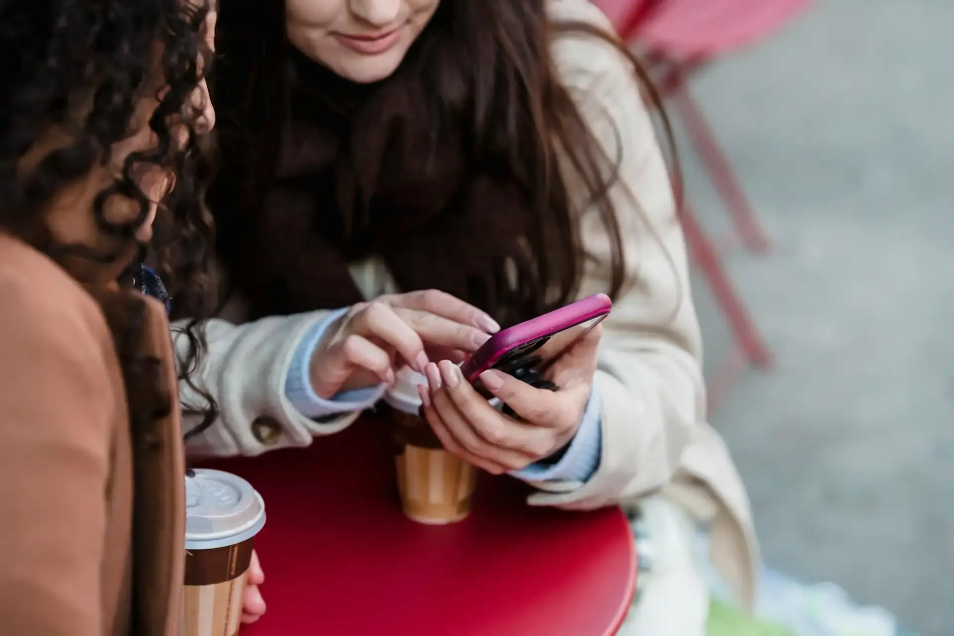 Two women sitting at an outdoor café, checking eSIM settings on a smartphone before traveling abroad