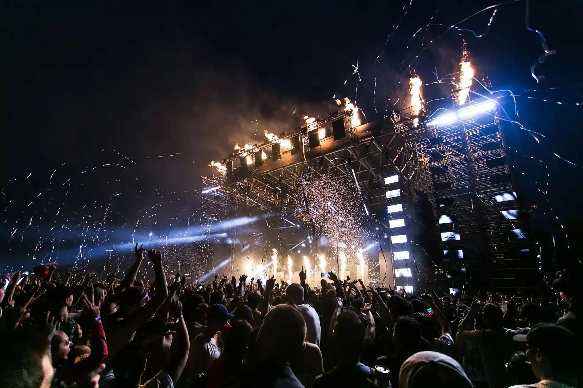 Energetic crowd at an outdoor concert with stage lights and fireworks, capturing the excitement of planning a music-focused trip to Asia.