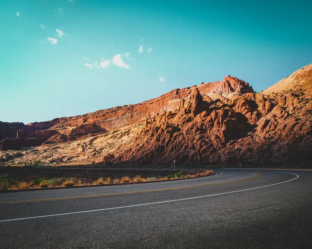 Scenic highway winding through red rock desert cliffs in the American Southwest, a popular USA road trip route with clear blue skies.