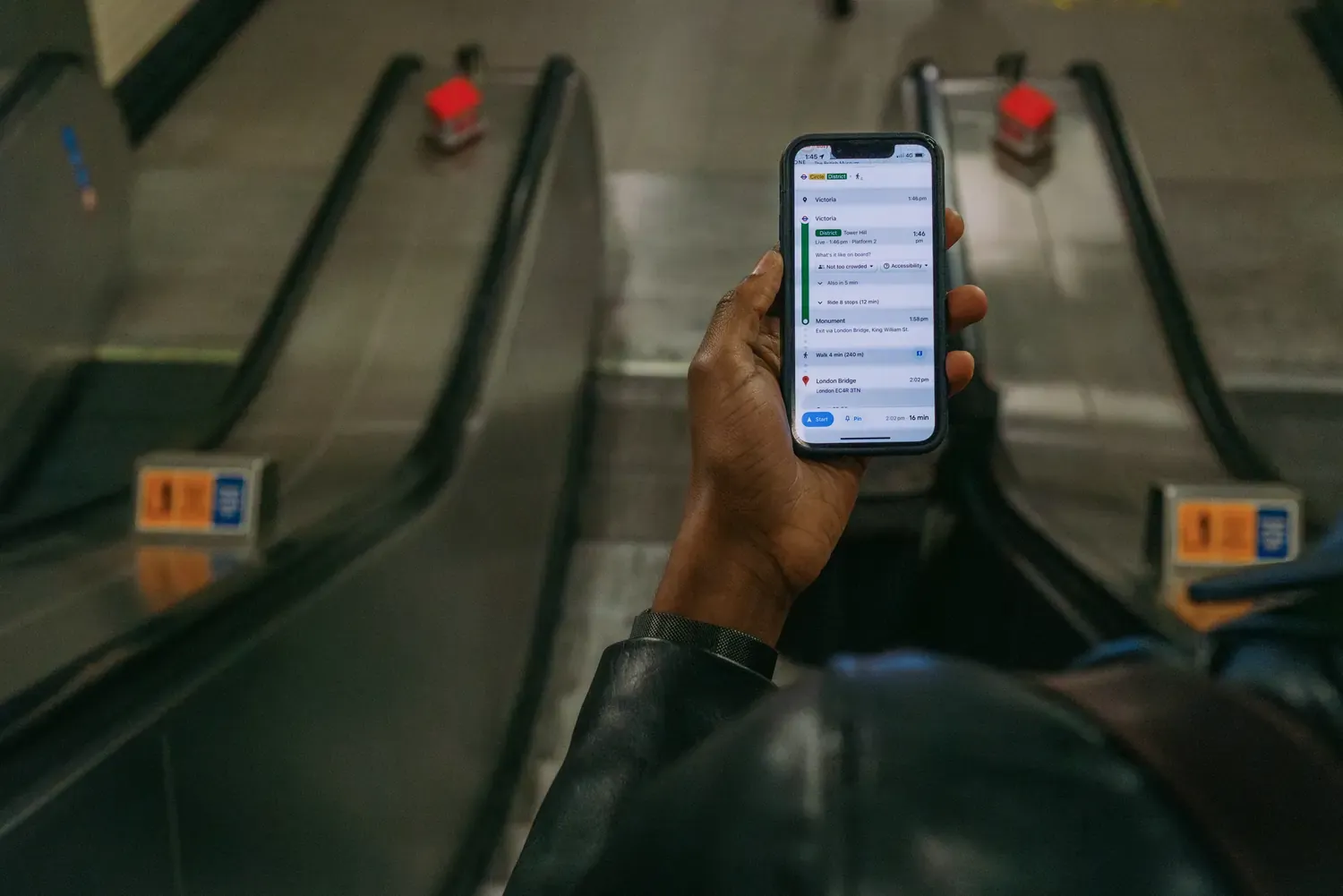 Traveler checking directions to London Bridge on a smartphone while riding an escalator.