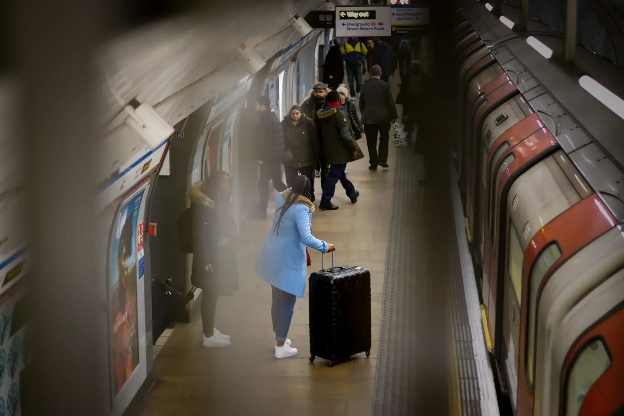 Traveler with a suitcase waiting on a London Underground platform beside a Tube train.