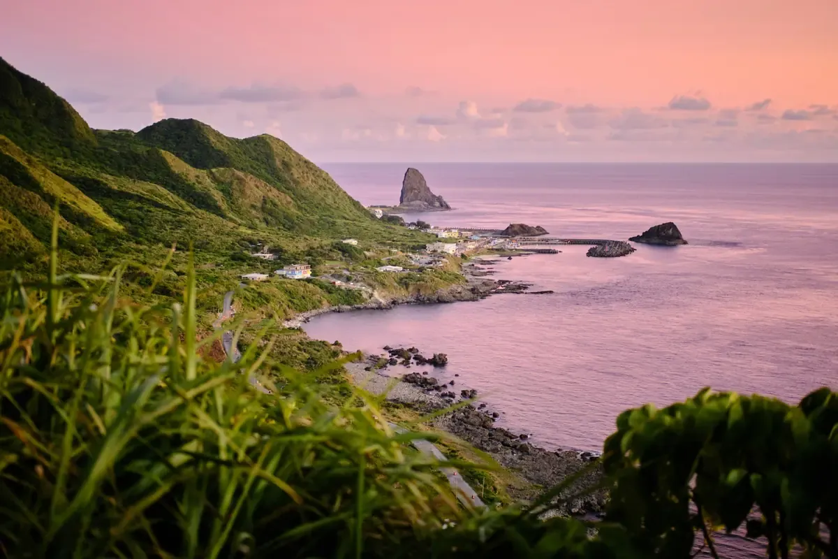Mountainous coastline and rocky sea stacks beneath a pink sunset sky in Taiwan.