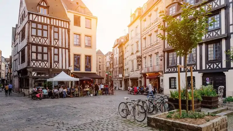 Charming European street with half-timbered buildings, outdoor cafés, and parked bicycles at sunset.