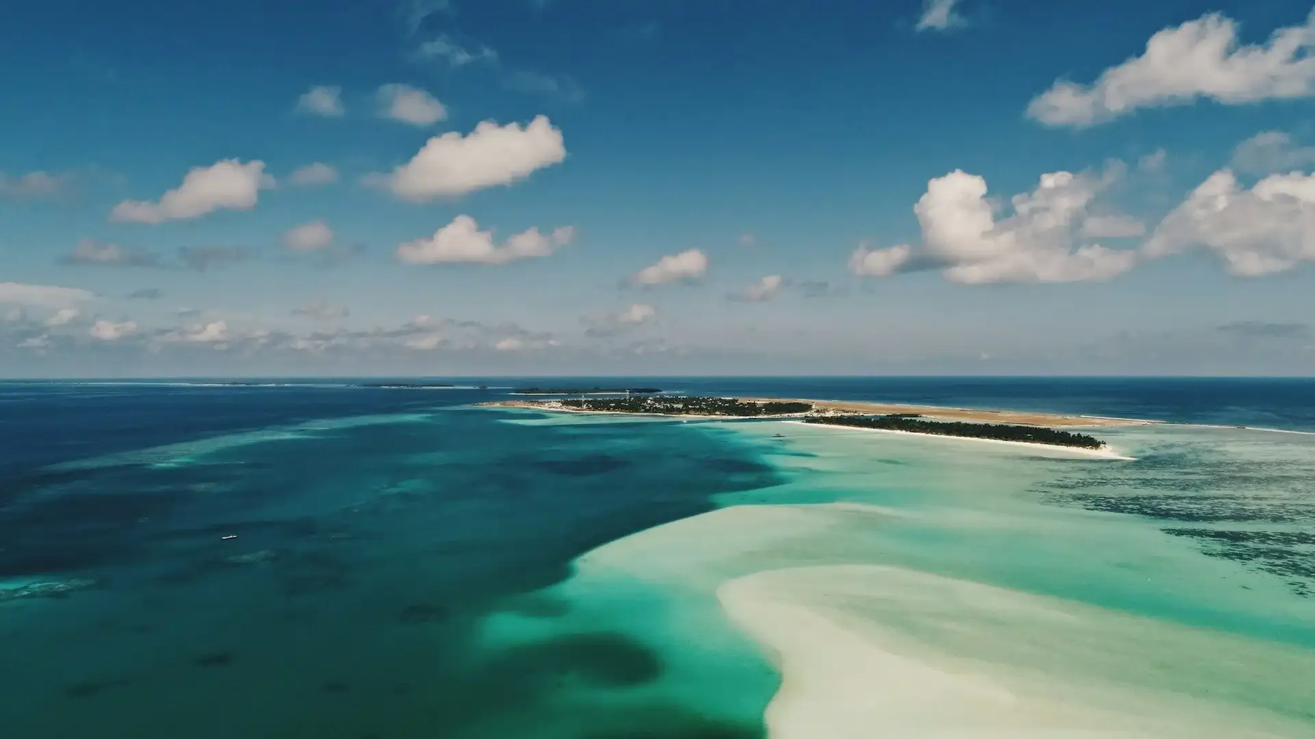 Aerial view of a remote tropical island surrounded by vibrant turquoise waters and coral reefs in the Indian Ocean.