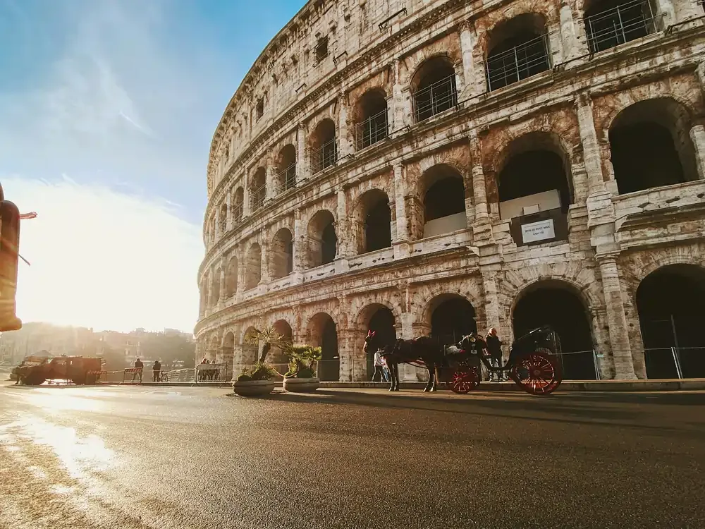 The Colosseum in Rome viewed from street level, with its arched stone façade lit by warm daylight.