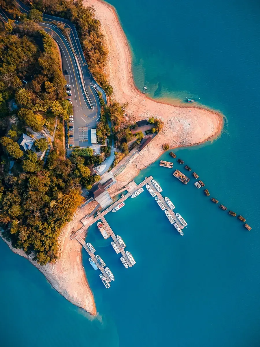 Aerial view of a marina in Sun Moon Lake with boats beside a winding coastal road and turquoise water.